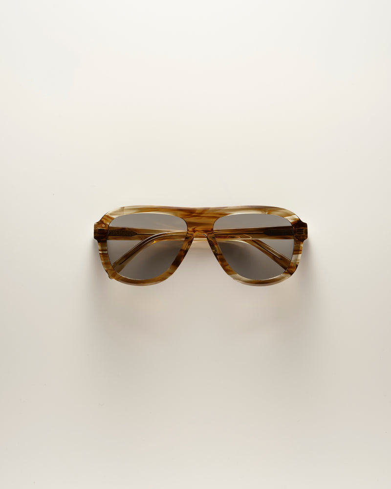 A pair of oversized square sunglasses with a translucent brown and amber tortoiseshell acetate frame and dark tinted lenses, photographed from directly above on a clean off-white background.