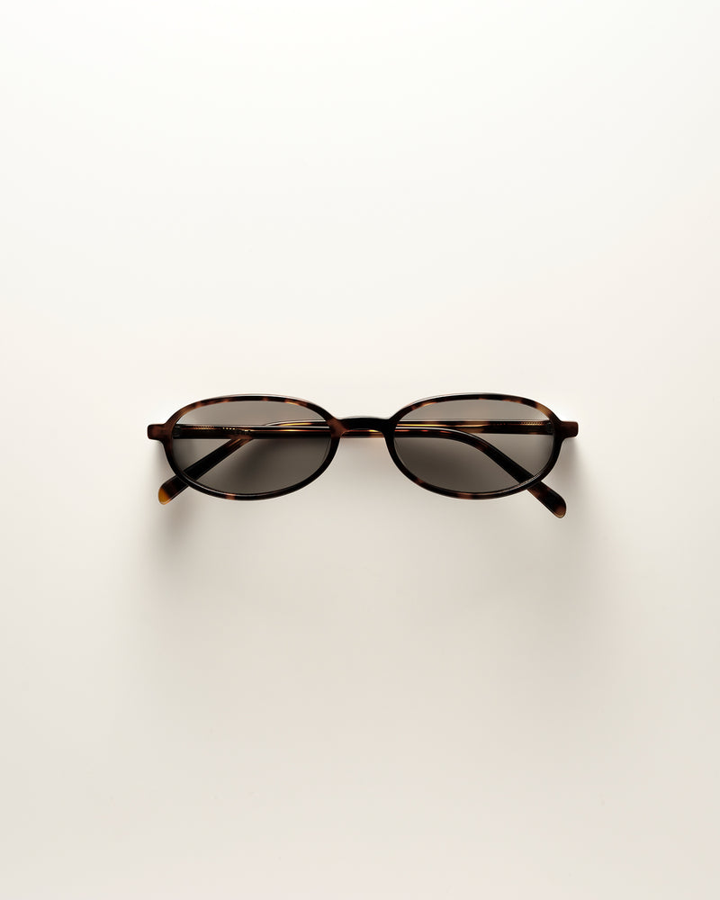 Oval eyeglasses with a tortoiseshell frame and dark tinted lenses, photographed from above on a clean white background.